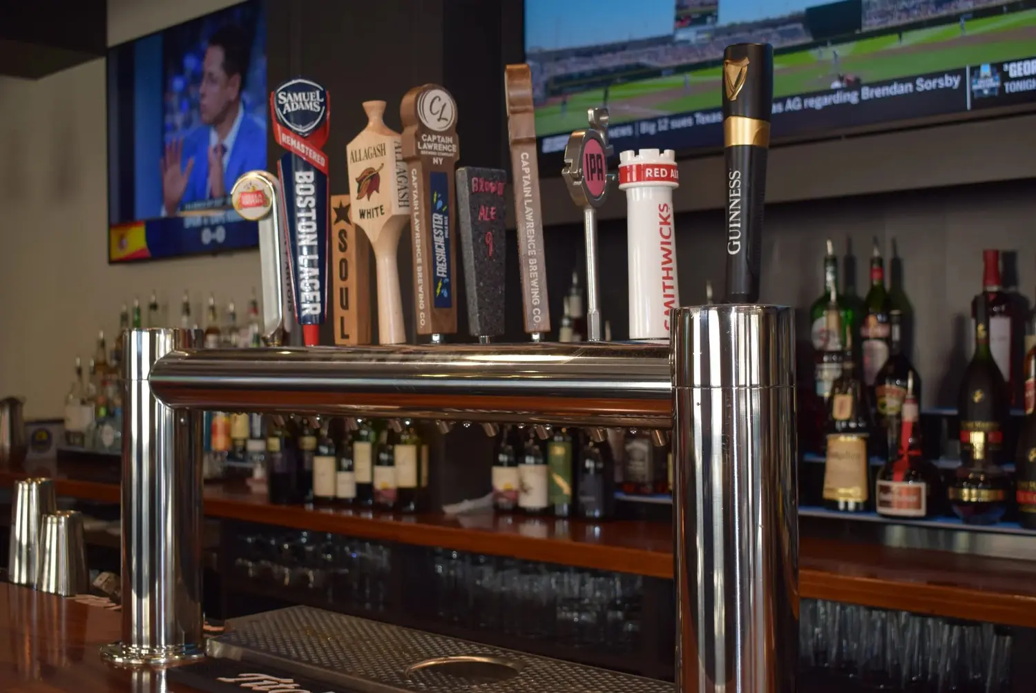 The tap tower at the bar with the game on behind it.
