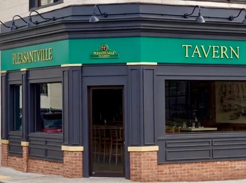 The tavern's corner storefront: dark panels, brick base and a green sign band with brass Pleasantville and Tavern lettering.